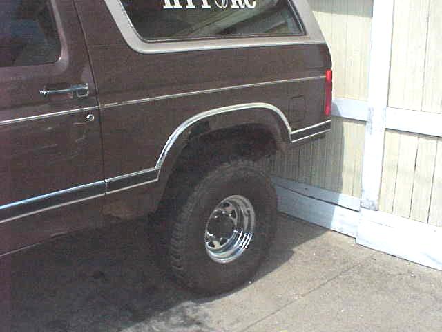 Maroon Ford Bronco rear quarter, lifted on chrome wheel, parked by building