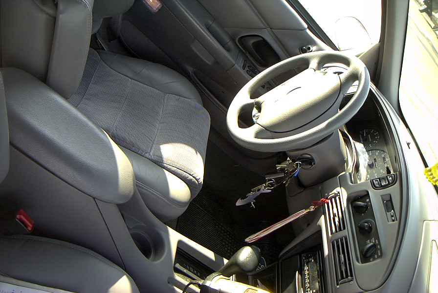 Front interior of a van showing gray cloth seats, four-spoke wheel and column shifter with Ford key