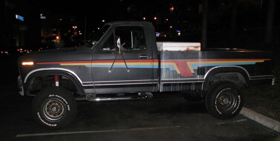 Lifted dark Ford pickup with rainbow stripe graphics and BFGoodrich all-terrain tires, side view at night