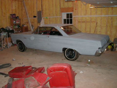 1965 Mercury Comet - Primer-painted 1965 Mercury Comet coupe sits in a garage, red interior parts scattered nearby.