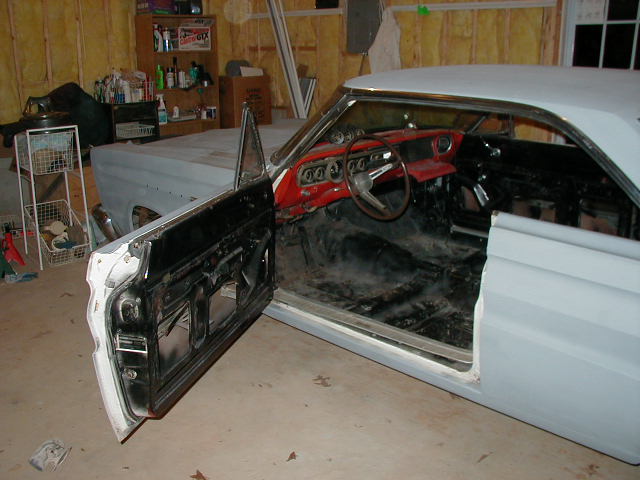 Primer-white coupe body shell with open door showing red dash in a garage restoration