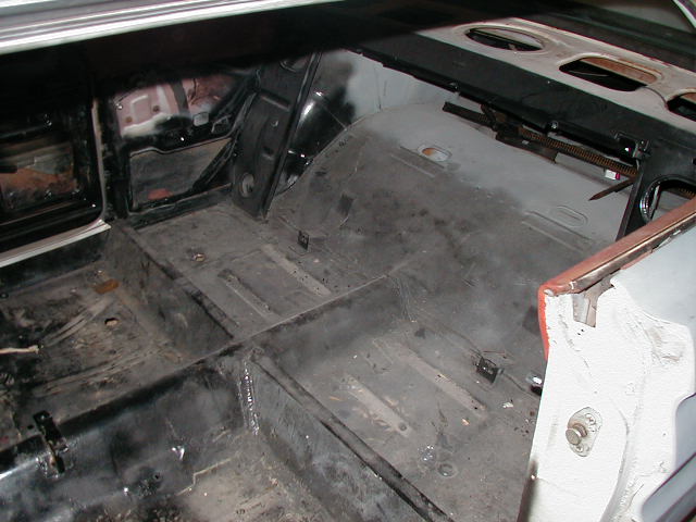Gutted car interior showing bare floor pans and transmission tunnel during restoration.
