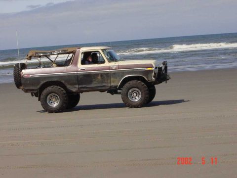1996 Ford Bronco - A two-tone Ford Bronco is driven on the beach near the ocean waves.