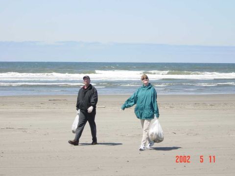 1996 Ford Bronco - Two individuals participate in a beach cleanup, collecting debris along the shore under a bright sky.