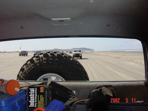 1996 Ford Bronco - Several vehicles are driving on a wide, sandy beach with the ocean in the background.