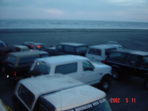 1996 Ford Bronco - Several Ford Bronco SUVs are parked on a beach near the ocean.