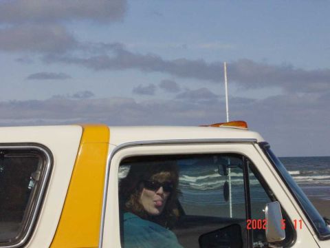 1996 Ford Bronco - A woman sticks her tongue out from the interior of a white and yellow SUV, with the ocean visible behind. A watermark indicates the photo w…