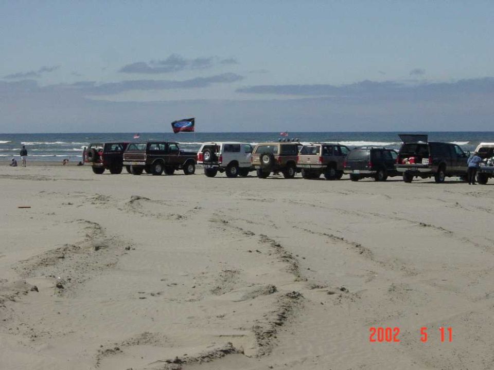 Row of full-size Broncos and 4x4 trucks parked along the surf at a beach run, 2002