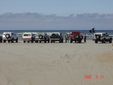1996 Ford Bronco - Several Ford Broncos are parked on a sandy beach near the ocean.