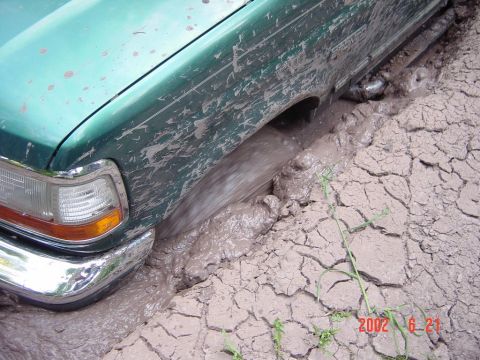 1996 Ford Bronco - A green SUV is stuck in thick mud, with water splashing around the front wheel.