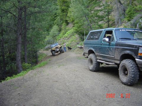 1996 Ford Bronco - A dark green 1996 Ford Bronco is parked on a dirt road, with another off-road vehicle visible further up the incline.