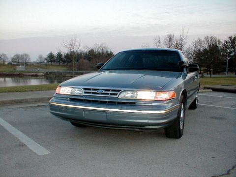 1995 Ford Crown Victoria - A 1995 Ford Crown Victoria is parked outdoors near a body of water under an overcast sky.