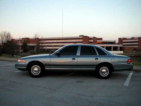 1995 Ford Crown Victoria - A silver 1995 Ford Crown Victoria sedan is parked in front of a brick building.