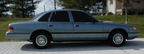 1995 Ford Crown Victoria - A light blue 1995 Ford Crown Victoria sedan is parked outdoors on a paved surface.