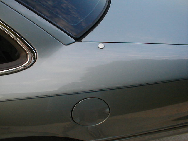 Silver car rear quarter panel showing a round flush button above the fuel filler door