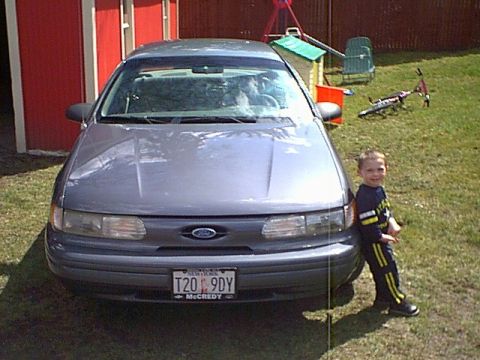 1993 Ford Taurus - A young boy poses next to a 1993 Ford Taurus in a residential backyard.