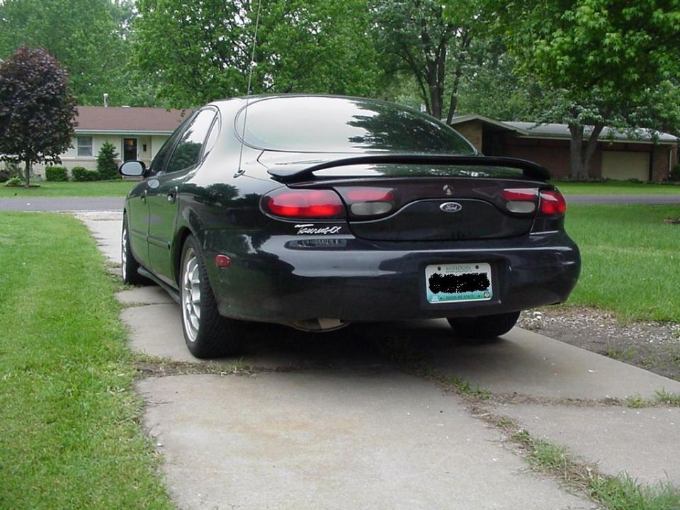 Black Ford Taurus sedan viewed from rear on a driveway with spoiler and alloy wheels.