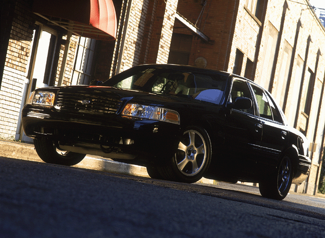 Lowered black Ford Crown Victoria with five-spoke wheels on a brick-lined street, low angle