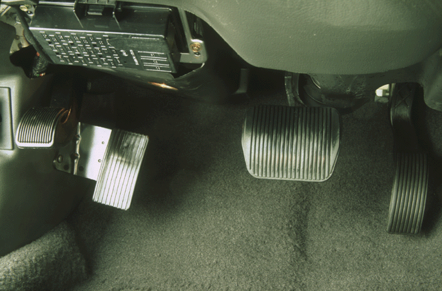 Car driver footwell showing brake and accelerator pedals with exposed fuse panel above