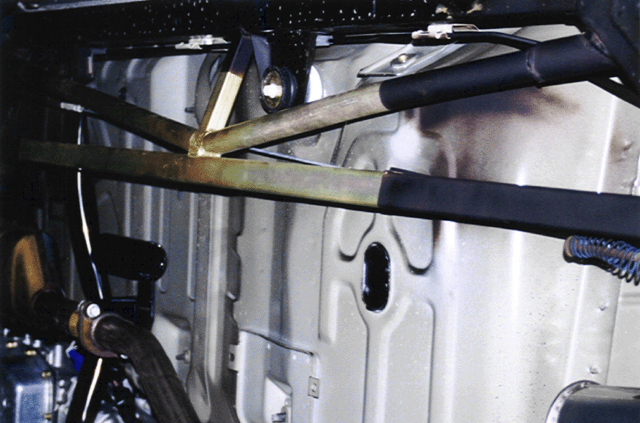 Roll cage bars with black padding and gold cross braces inside a stripped car body shell