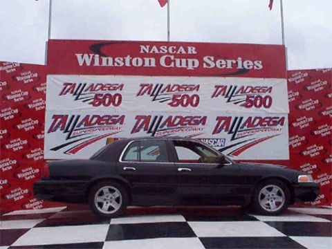 2001 Ford Crown Victoria - A black 2001 Ford Crown Victoria is displayed on a checkered floor with NASCAR Winston Cup Series banners in the background.