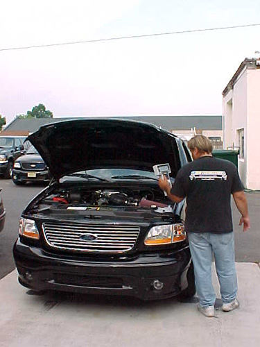 2001 Ford Crown Victoria - Man inspects the engine of a black 2000 Ford F-150 Lightning pickup truck parked outside.