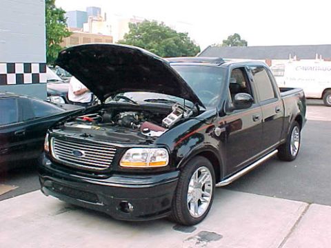 2001 Ford Crown Victoria - A black Ford F-150 SVT Lightning pickup truck is parked with its hood up, revealing the engine compartment.