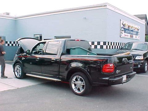 2001 Ford Crown Victoria - A black Ford F-150 pickup truck is parked outside a building with another truck behind it.