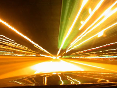 2001 Ford Crown Victoria - Long-exposure night shot taken over a car's hood on a lit highway, with streetlights, signs and taillights stretched into streaks convergin…