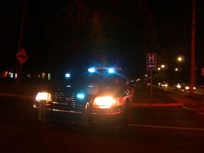 2001 Ford Crown Victoria - Night shot of a police-style sedan at a roadside with headlights on and blue-and-white emergency lights flashing from a roof-mounted lightb…