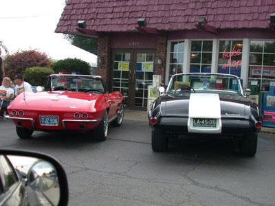 2001 Ford Crown Victoria - Rear view of two classic convertibles parked side by side at a drive-in style storefront: a red mid-1960s Chevrolet Corvette Sting Ray road…