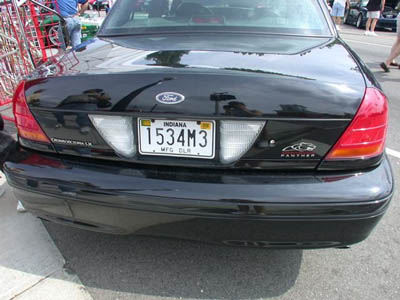 2001 Ford Crown Victoria - Close rear view of a black Ford Crown Victoria LX trunk lid at an outdoor event, showing the Ford oval badge, an Indiana MFG DLR plate read…