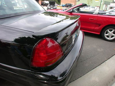 2001 Ford Crown Victoria - Close-up of the right rear quarter and taillight of a glossy black Ford Crown Victoria fitted with a raised trunk-lid spoiler, shot in a lo…