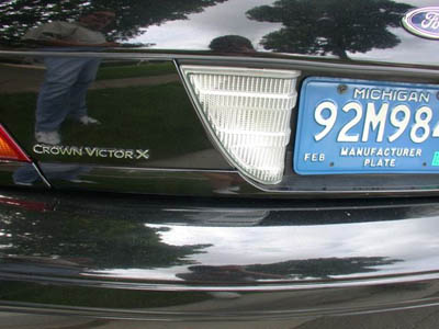 2001 Ford Crown Victoria - Close-up of the rear of a black Ford Crown Victoria showing a 'Crown Victor X' badge and Ford oval on the trunk, a backup light, and a blue…