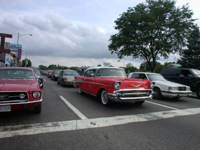 2001 Ford Crown Victoria - Red and white 1957 Chevrolet Bel Air cruising a multi-lane street during a cruise-in, shot from the 3/4 front with its chrome bumper, hood…