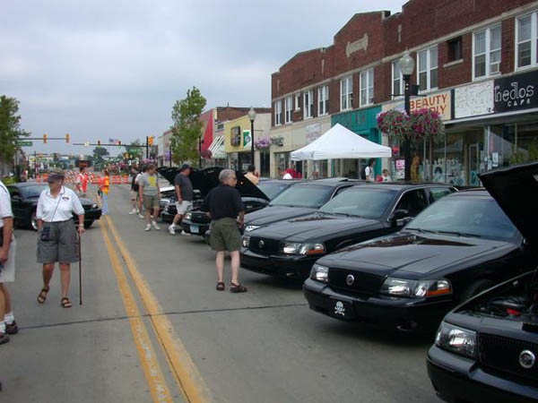 Row of black sedans with open hoods at a street car show