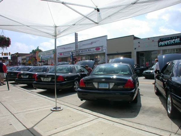 Row of black Ford Crown Victoria sedans parked under a white tent on a city street
