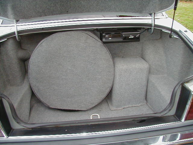 Open carpeted sedan trunk with spare tire cover and rear-mounted electronic unit