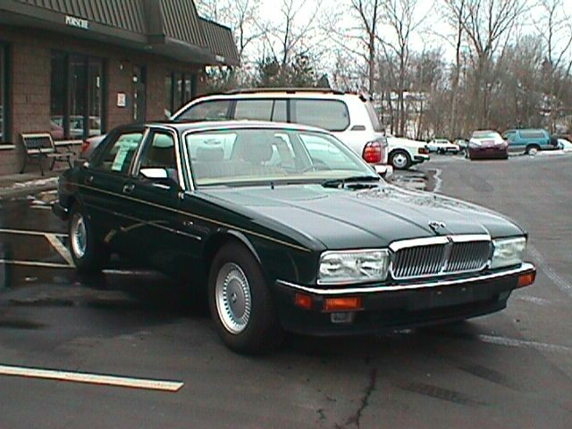 Dark green Jaguar XJ40 sedan parked in lot outside Porsche dealer