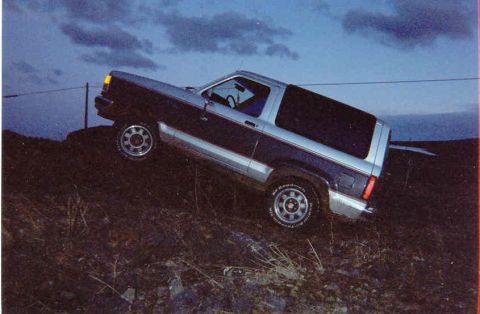 1989 Ford Bronco II - This 1989 Ford Bronco II is shown in a three-quarter front view, positioned on a grassy incline under a twilight sky.