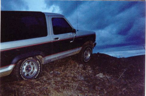 1989 Ford Bronco II - A two-tone Ford Bronco II is parked on a rocky incline with a dramatic cloudy sky overhead.