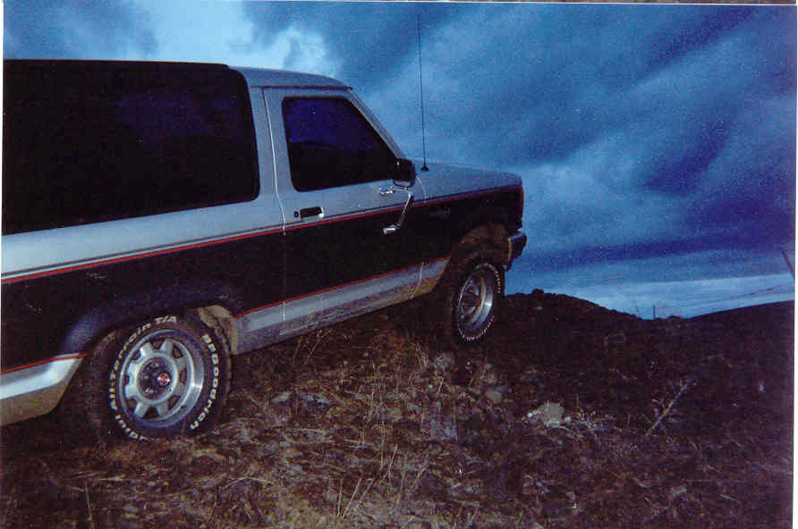 Black and silver two-door SUV parked on a rocky mound under a dark cloudy sky.