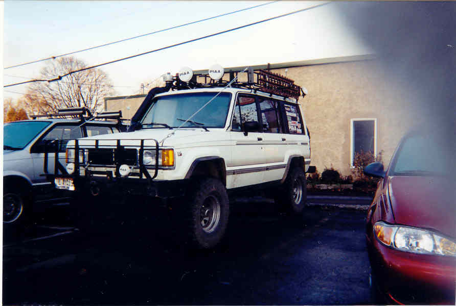 Lifted white SUV with roof rack, PIAA lights, brush guard and big off-road tires parked in a lot