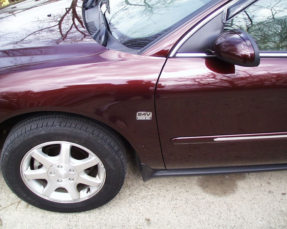 Side view of dark red sedan front fender, alloy wheel, and 24V DOHC badge