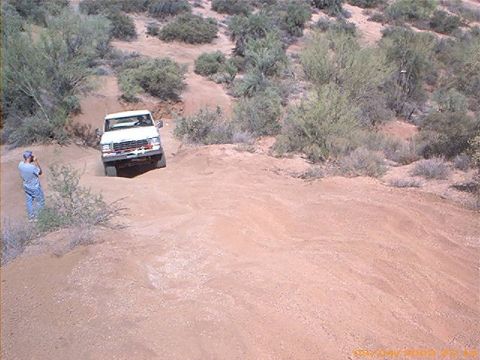 1979 Ford Bronco - A white Ford Bronco navigates a dusty, off-road trail with desert scrub brush.