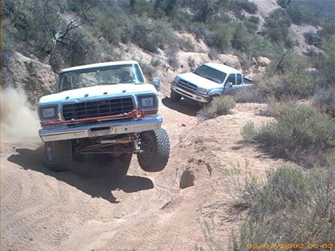 1979 Ford Bronco - Two trucks navigate a dusty, off-road trail with steep inclines and sparse vegetation.