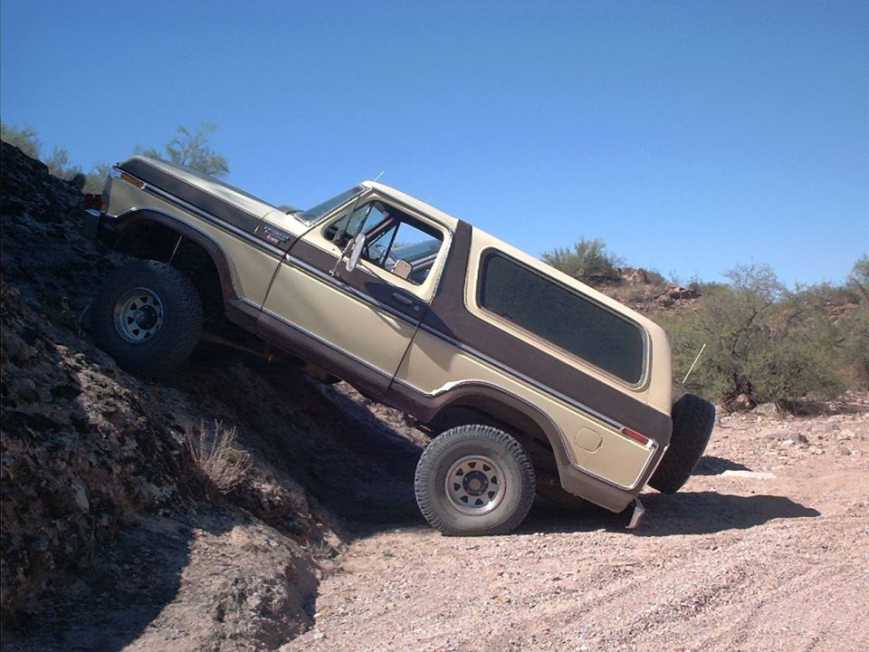 Tan and brown Ford Bronco SUV climbing a rocky ledge in the desert