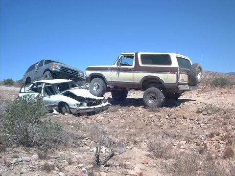 1979 Ford Bronco - Lifted two-tone tan-and-brown full-size Ford Bronco with woodgrain trim and a swing-out rear spare carrier, seen in profile crawling over r…