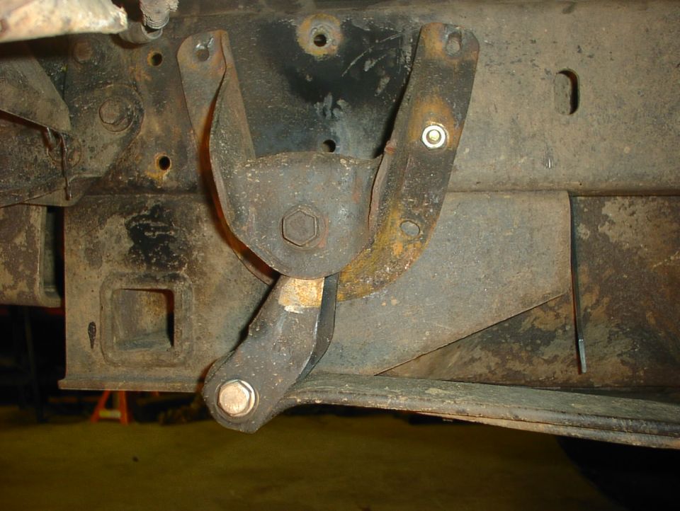 Rusty leaf spring shackle and hanger bracket bolted to a truck frame rail, viewed from underneath
