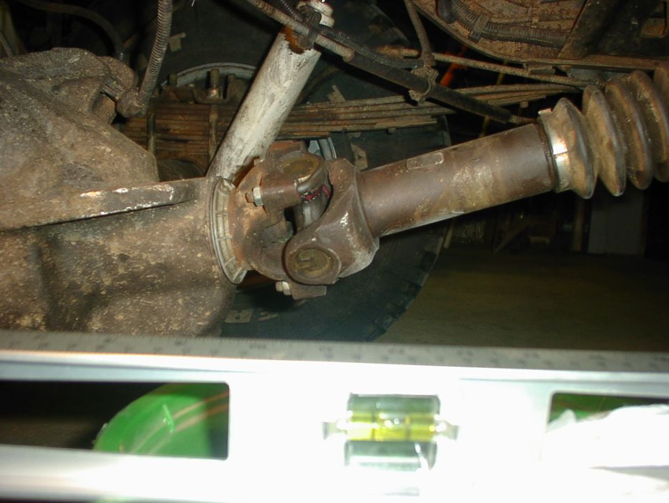 Underside view of driveshaft U-joint at rear axle yoke with level tool in foreground